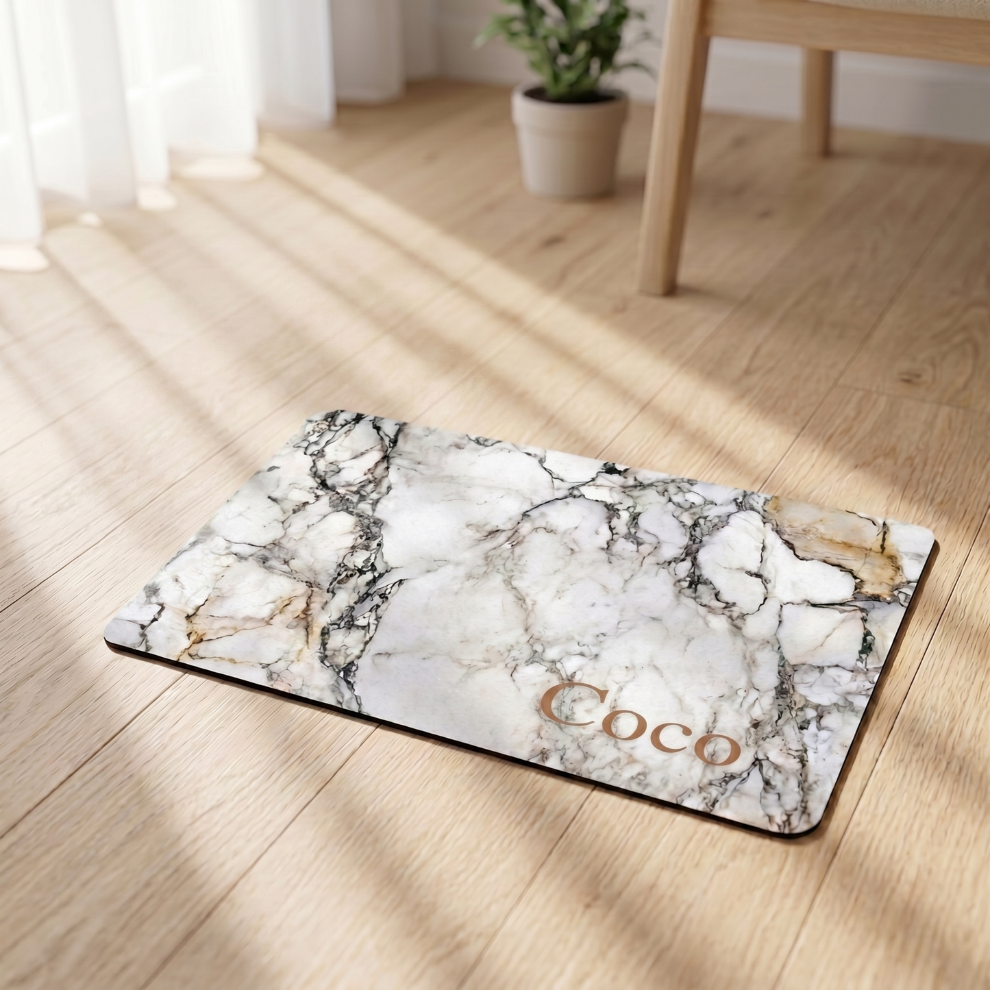 Marble-patterned dog food mat with 'Coco' on a wooden floor