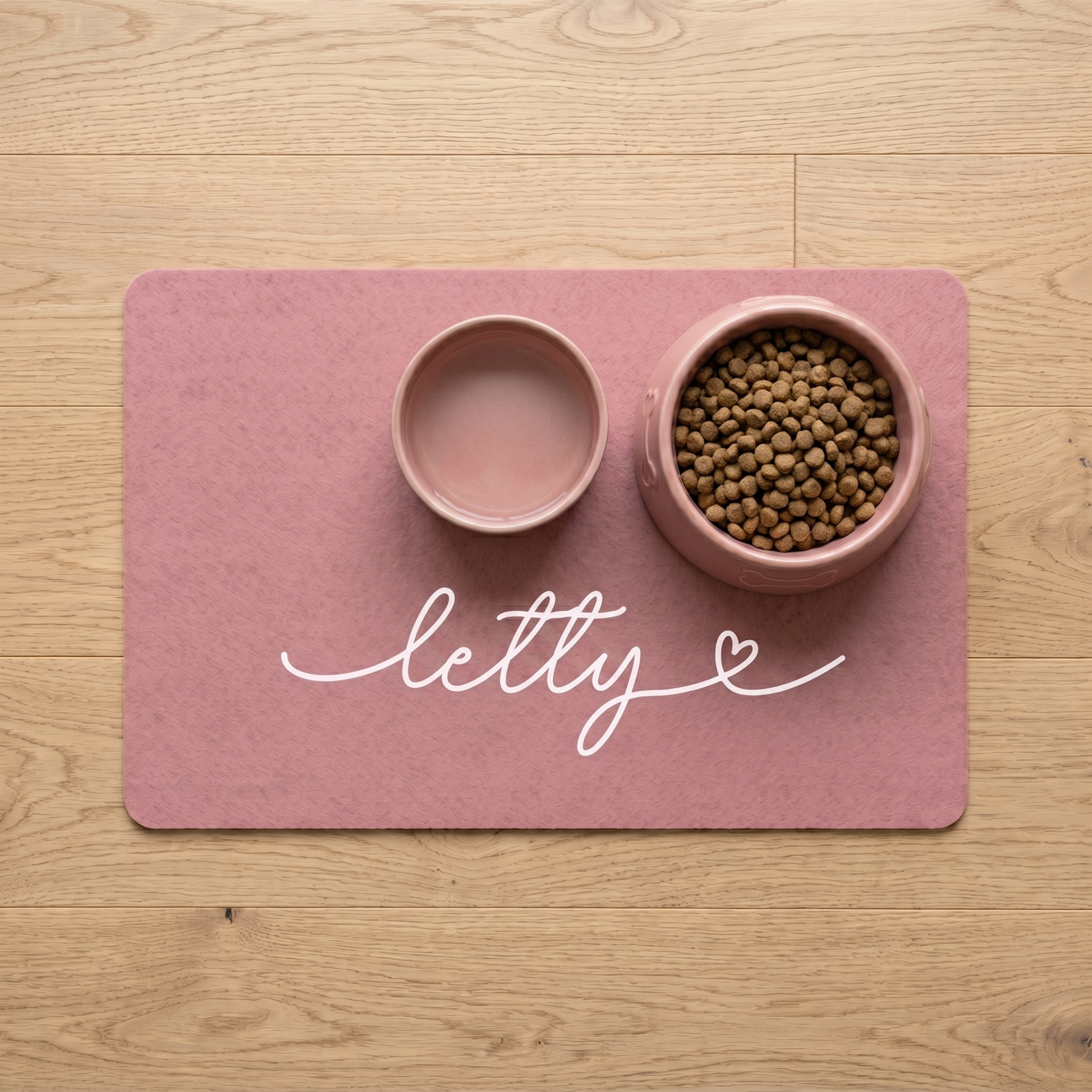 Pink pet mat with two bowls, one empty and one with food, on a wooden surface.
