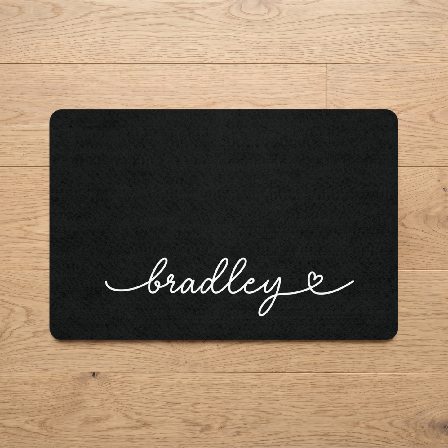 Black dog food mat with 'bradley' printed on a wooden floor