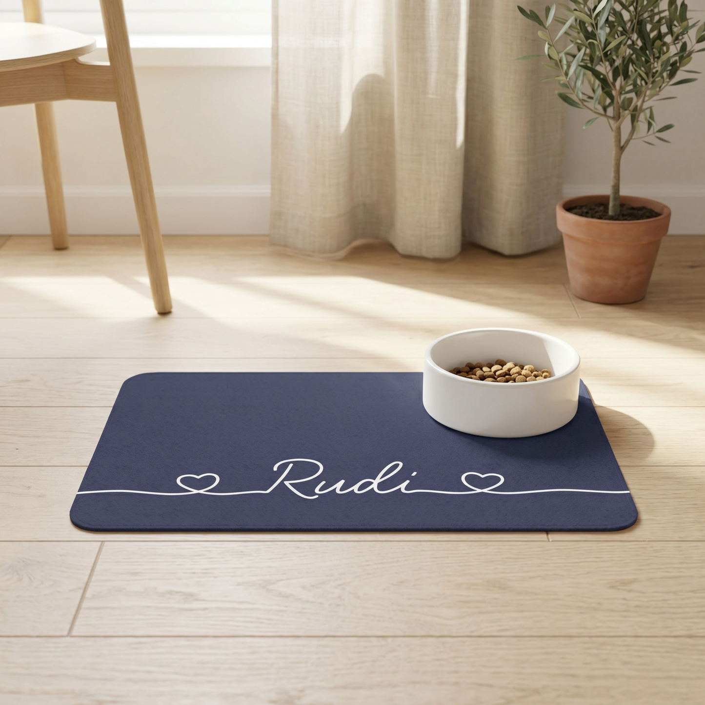 Navy blue dog food mat with 'Rudi' printed on it, featuring a white bowl with pet food on a wooden floor.