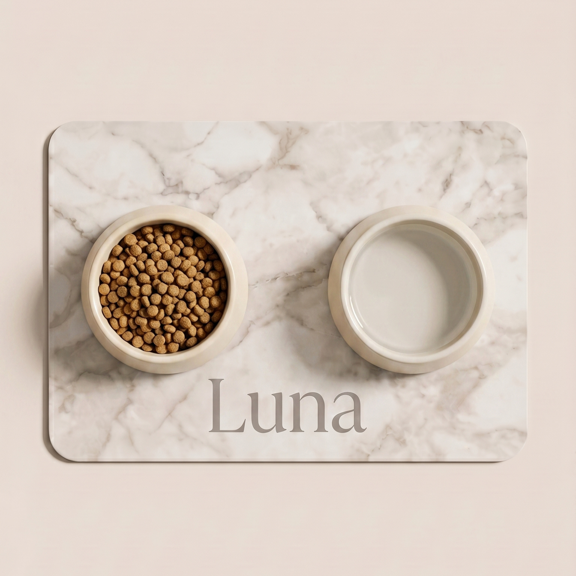 Two pet bowls on a marble placemat with 'Luna' engraved, one containing kibble and the other empty.