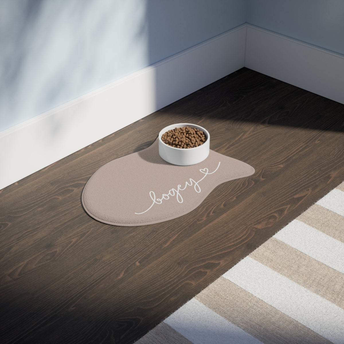 Beige fish-shaped personalized pet feeding mat with a food bowl on a dark wooden floor in sunlight