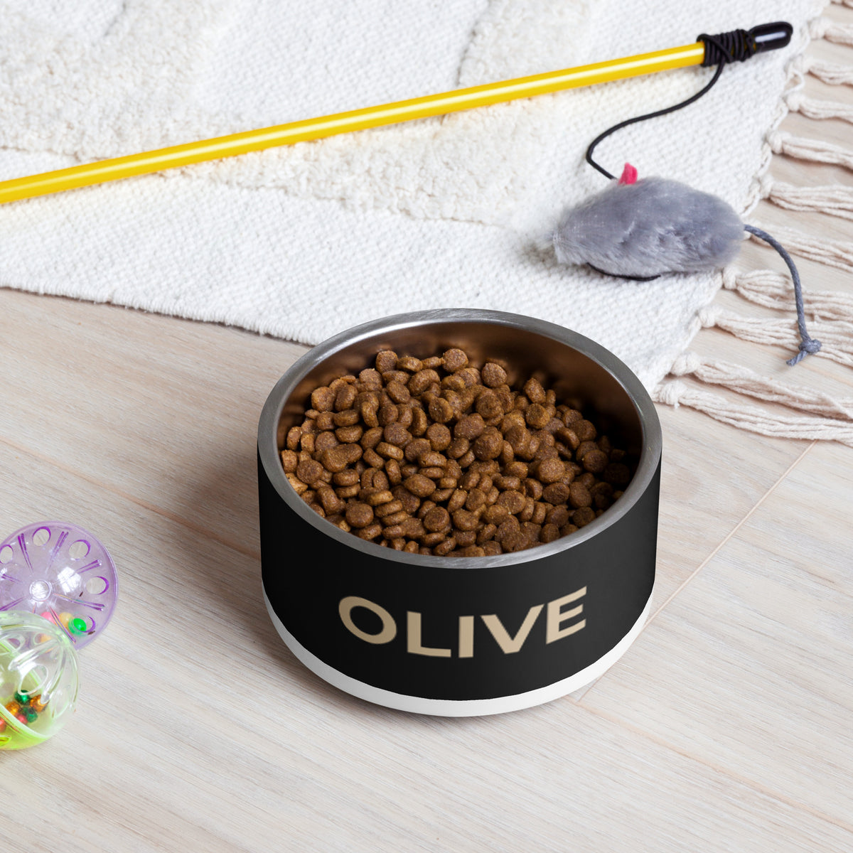 Black and gold modern personalized dog bowl filled with kibble on a rug next to a pet toy