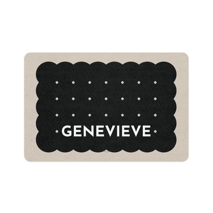 Black biscuit personalized dog food mat shaped like a scalloped cookie with dots and the name Genevieve on a sand background