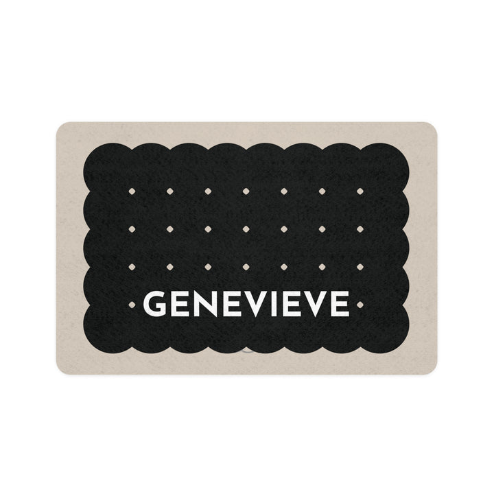 Black biscuit personalized dog food mat shaped like a scalloped cookie with dots and the name Genevieve on a sand background