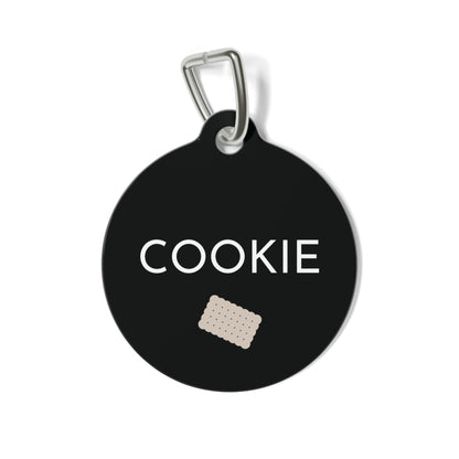 Round black biscuit personalized dog tag with the name Cookie in white capitals and a small sand scalloped biscuit