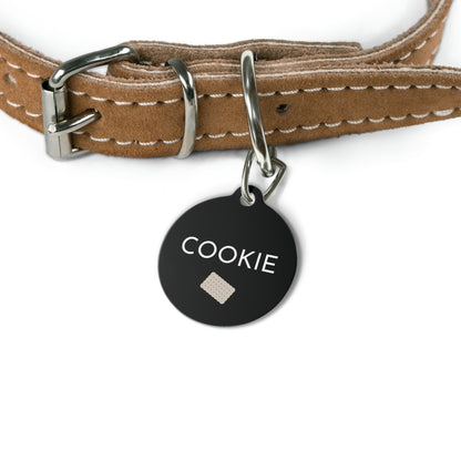 Black biscuit personalized dog tag hanging from a tan leather dog collar