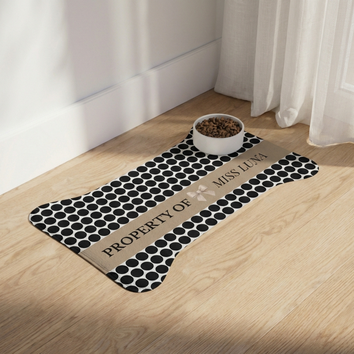 Black polka dot bone-shaped personalized pet feeding mat with a food bowl on a light wooden floor