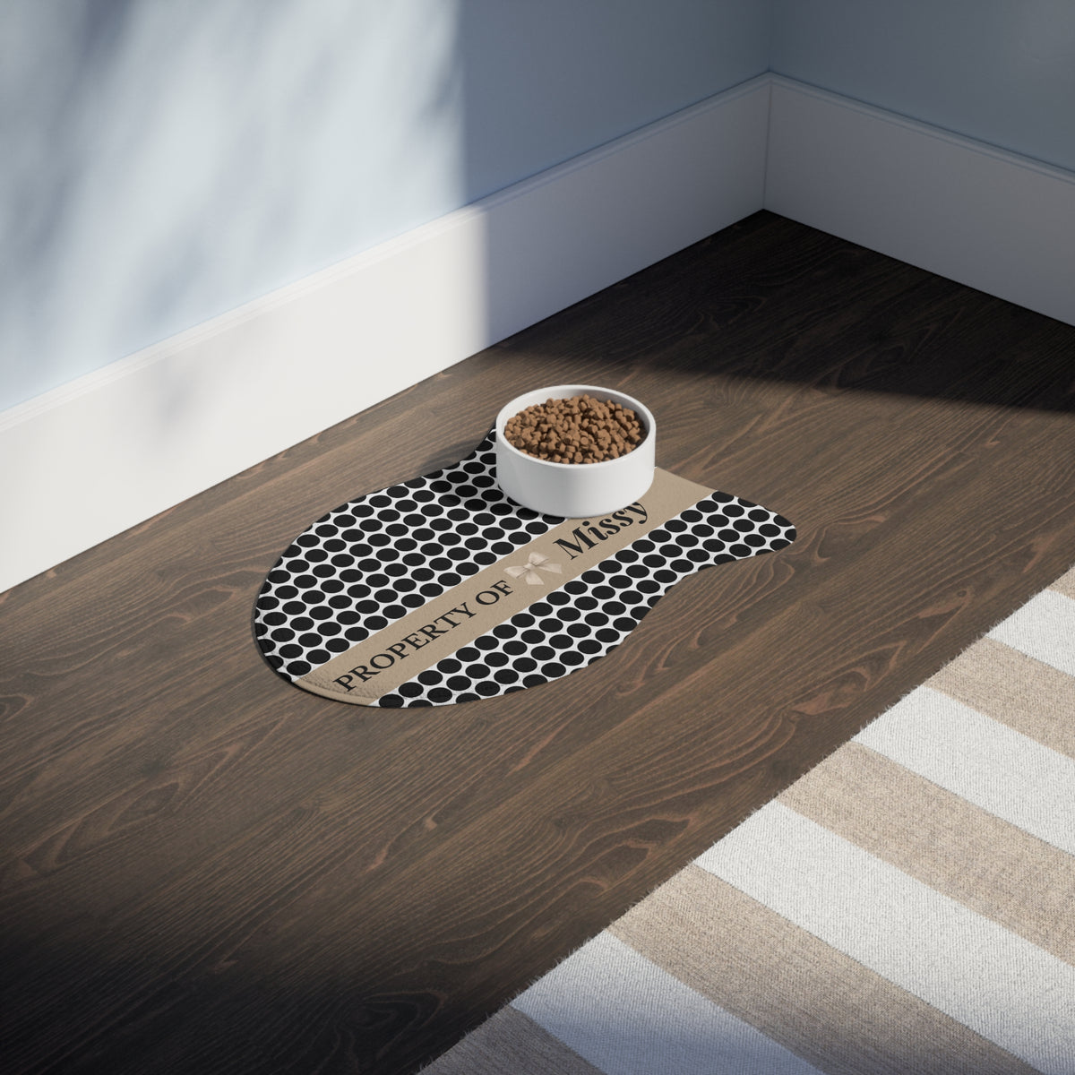 Black polka dot fish-shaped personalized feeding mat with a food bowl on a dark wooden floor