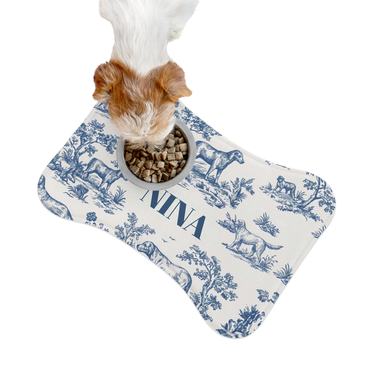 Small dog eating from a bowl on a blue toile bone-shaped personalized pet feeding mat, seen from above