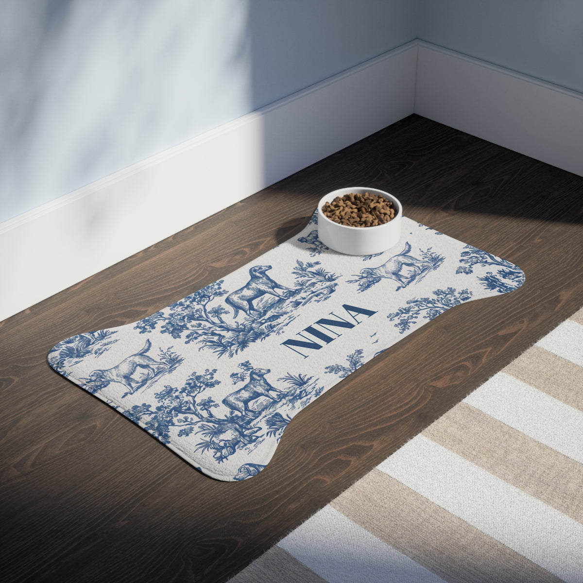 Blue toile bone-shaped personalized pet feeding mat with a bowl on a dark wooden floor