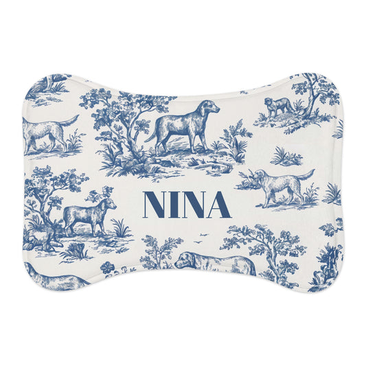 Blue toile bone-shaped personalized pet feeding mat with dogs in a classic toile landscape and the name Nina