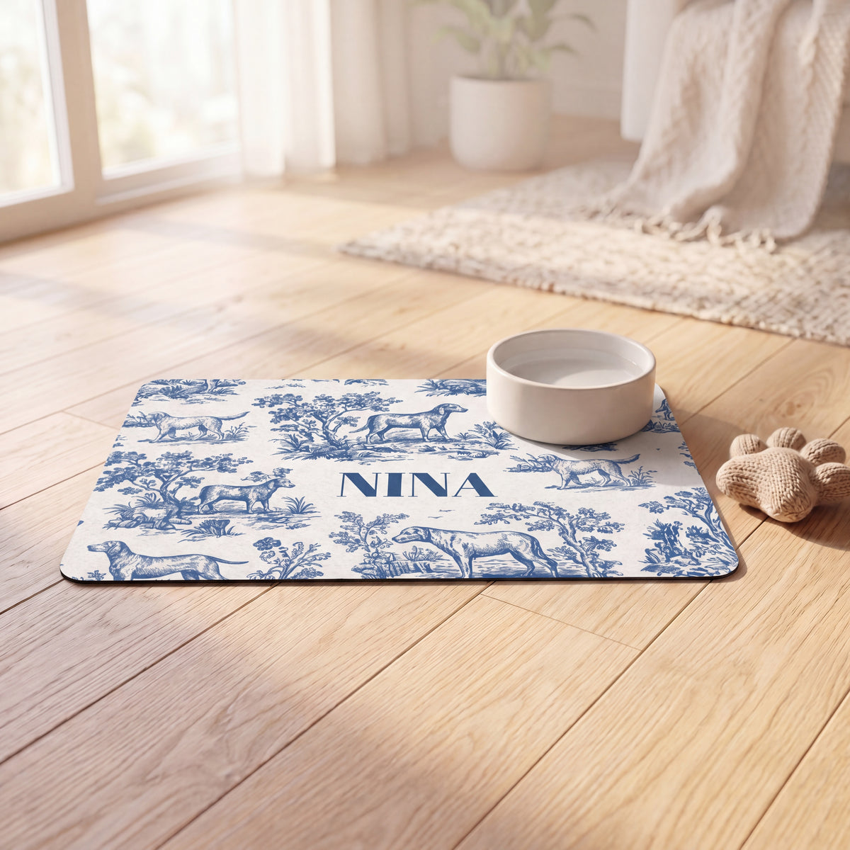 Blue toile personalized pet food mat with a bowl on a sunlit wooden floor