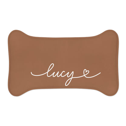 Small caramel bone-shaped personalized pet feeding mat with the name Lucy in white script