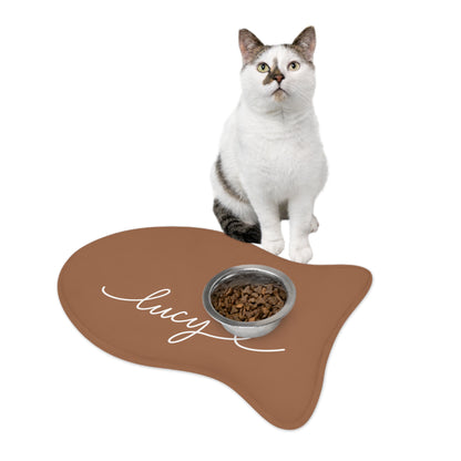 Cat sitting on a caramel fish-shaped personalized pet feeding mat next to a food bowl
