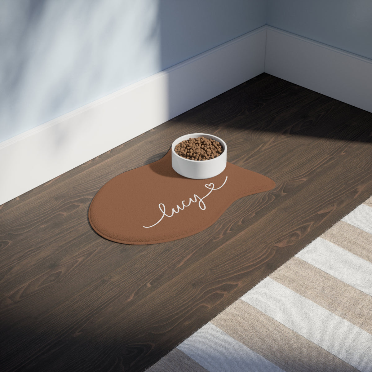 Caramel fish-shaped personalized pet feeding mat with a food bowl on a dark wooden floor in sunlight