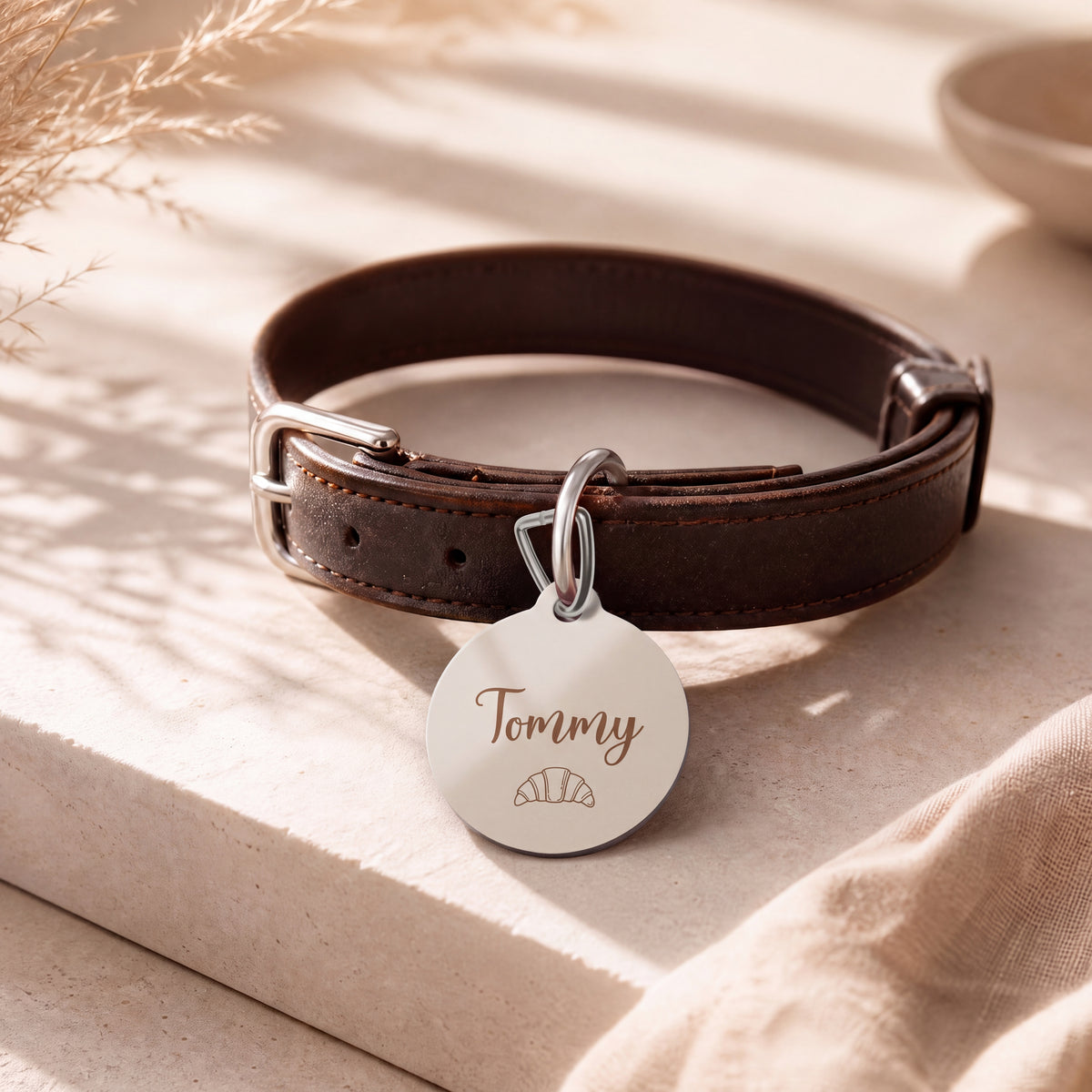 Croissant pet tag hanging from a dark brown leather dog collar