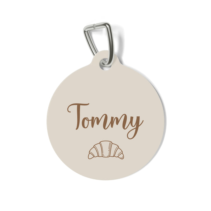 Cream personalized pet tag with the name Tommy in script and a small croissant