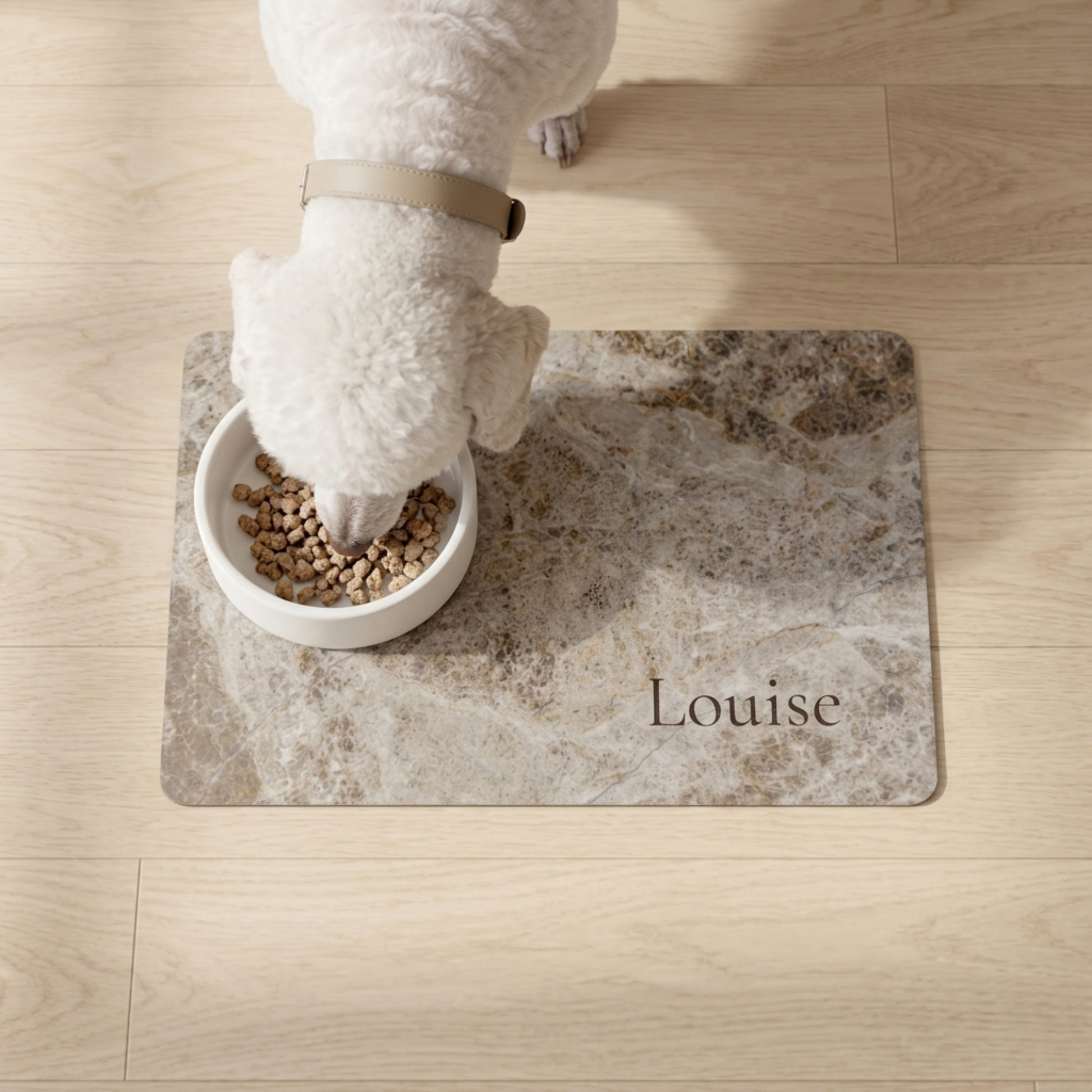 Dog eating from a bowl on a personalized dog food mat with 'Louise' printed on it.