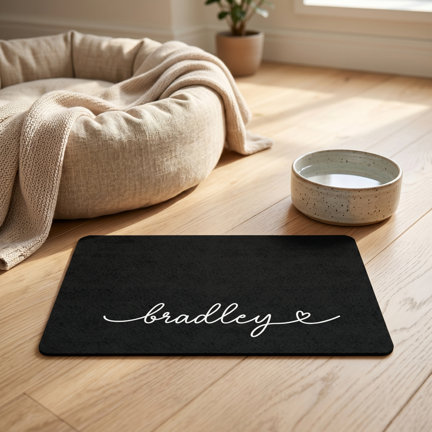 Pet bed with a blanket, water bowl, and personalized dog mat on a wooden floor.