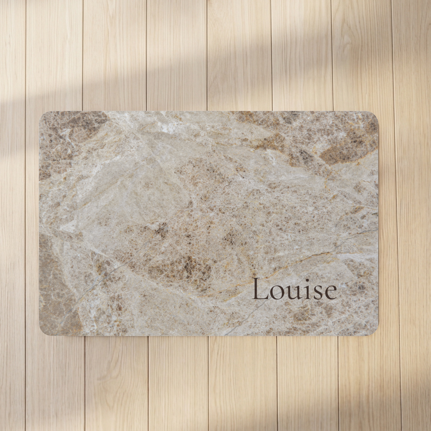 Marble-patterned dog bowl mat with 'Louise' on a wooden floor