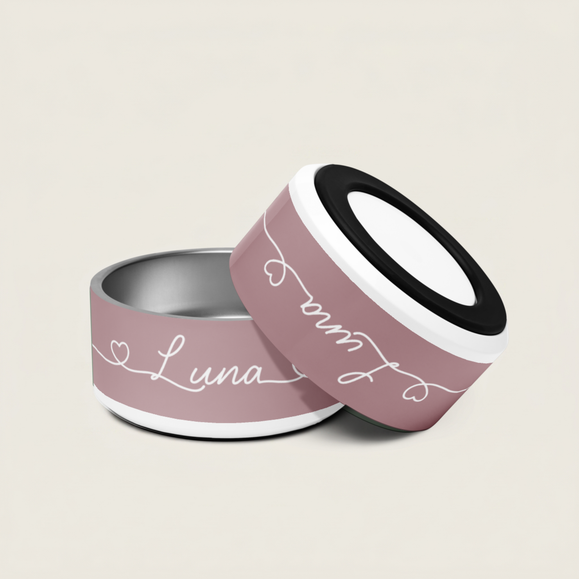 Two dog bowls, one pink with 'Luna' written on it, the other black and silver, on a beige background.