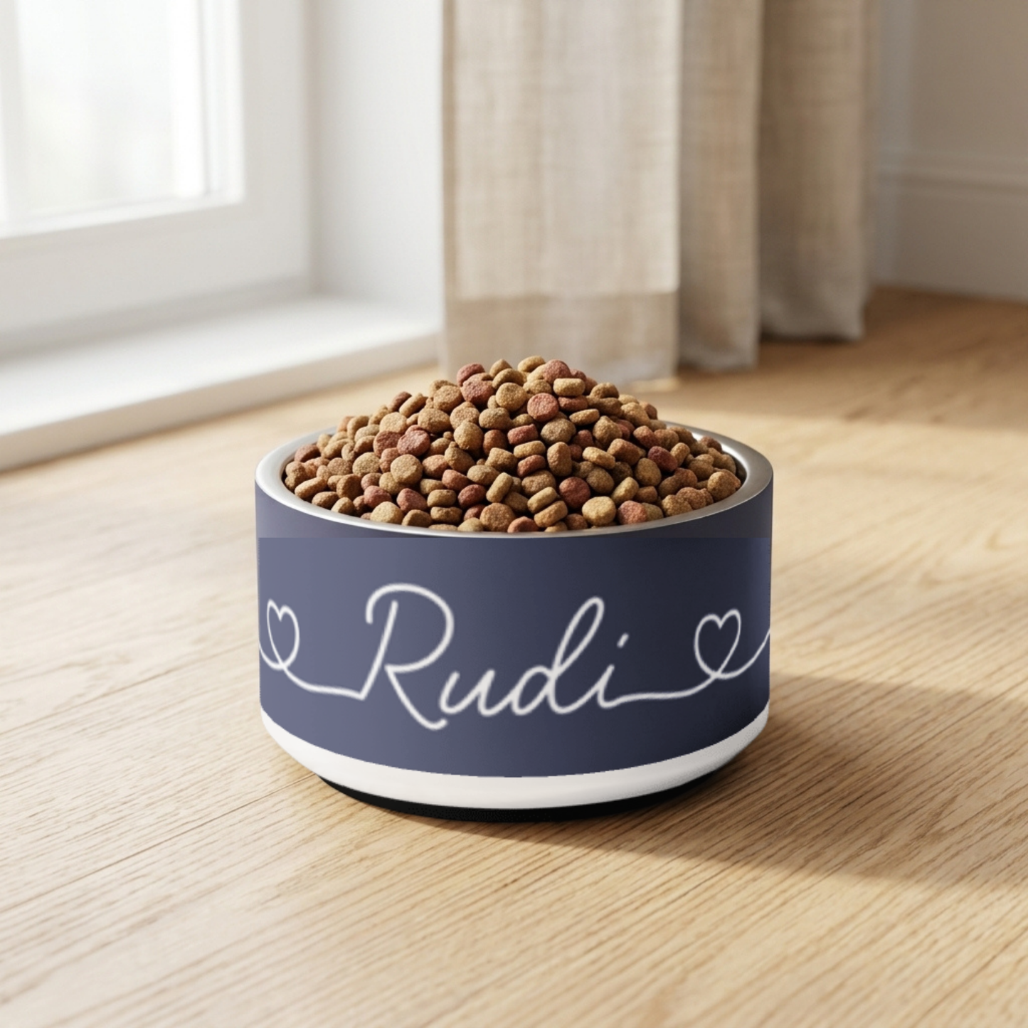 Navy blue pet food bowl labeled 'Rudi' with pet food on a wooden floor.