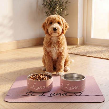Golden doodle puppy sitting behind two dusty rose personalized dog bowls on a pink feeding mat