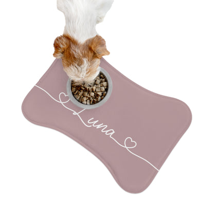Dog eating from a bowl on a dusty rose bone-shaped personalized feeding mat, seen from above