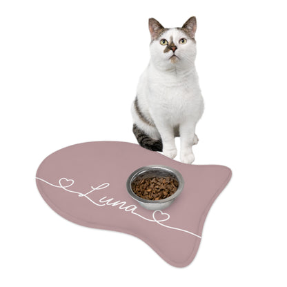 Black and white cat sitting on a dusty rose fish-shaped personalized feeding mat with a food bowl