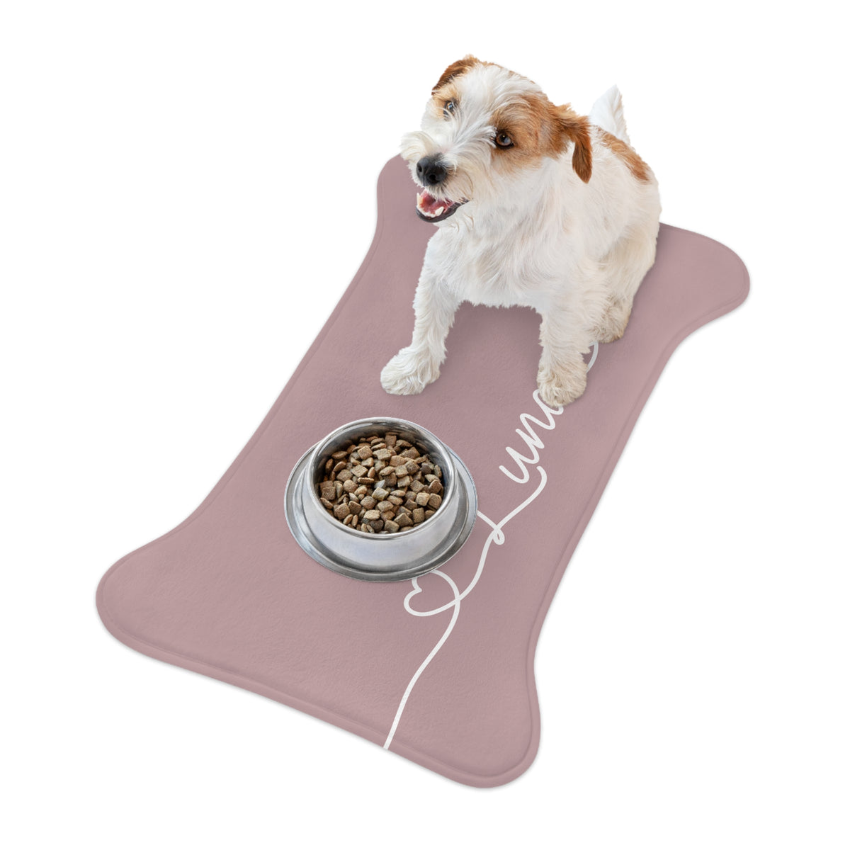 Jack Russell terrier sitting on a dusty rose bone-shaped personalized feeding mat next to its food bowl