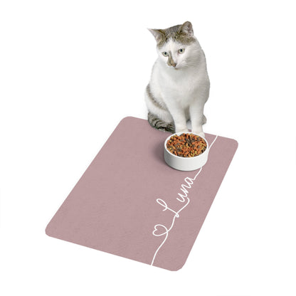 Cat sitting on a dusty rose personalized pet food mat next to a food bowl