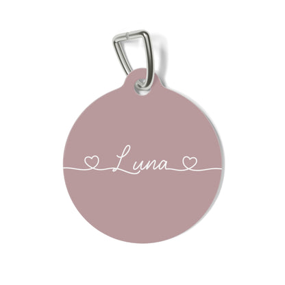 Round dusty rose personalized pet tag with the name Luna in white script between two small hearts