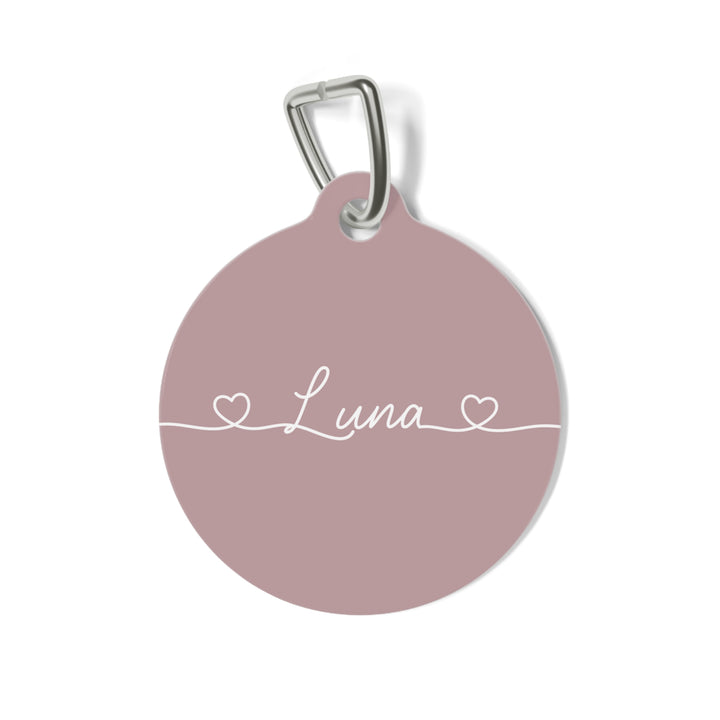 Round dusty rose personalized pet tag with the name Luna in white script between two small hearts