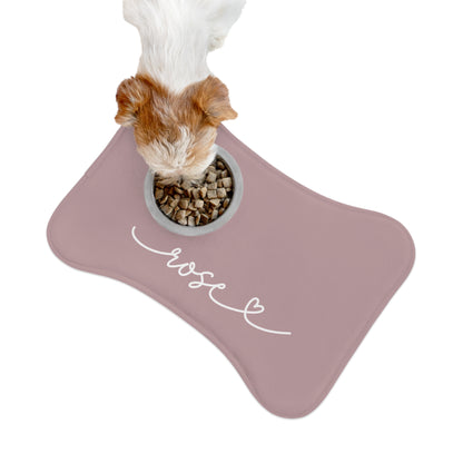 Small dog eating from a bowl on a dusty rose bone-shaped personalized pet feeding mat, seen from above