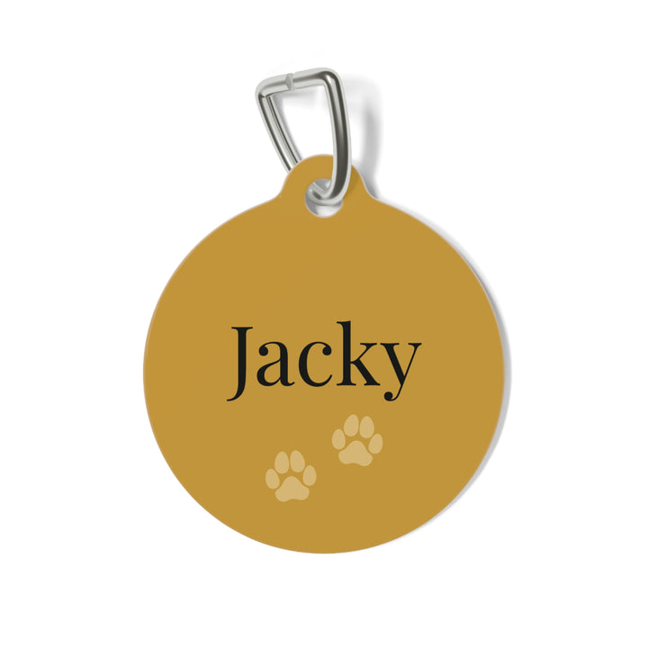 Round gold personalized dog tag with the name Jacky in dark serif lettering and two paw prints