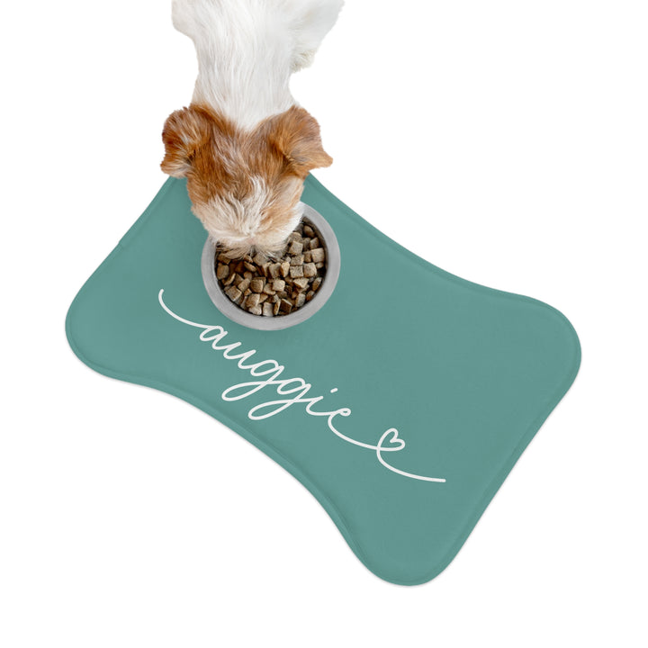 Fluffy dog eating from a bowl on a jade bone-shaped personalized pet feeding mat, seen from above