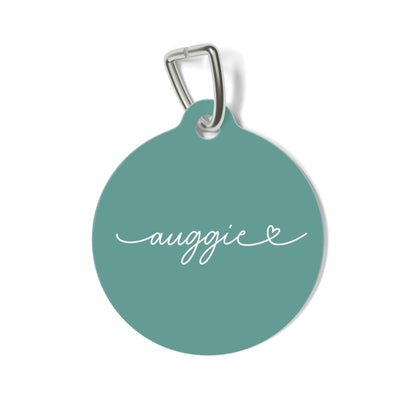 Round jade green personalized pet tag with the name Auggie in white handwritten script and a small heart