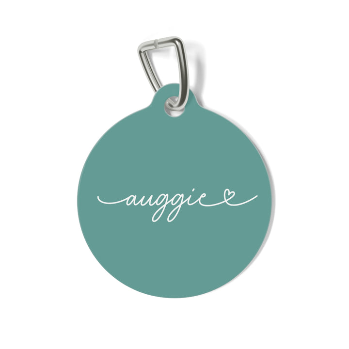 Round jade green personalized pet tag with the name Auggie in white handwritten script and a small heart
