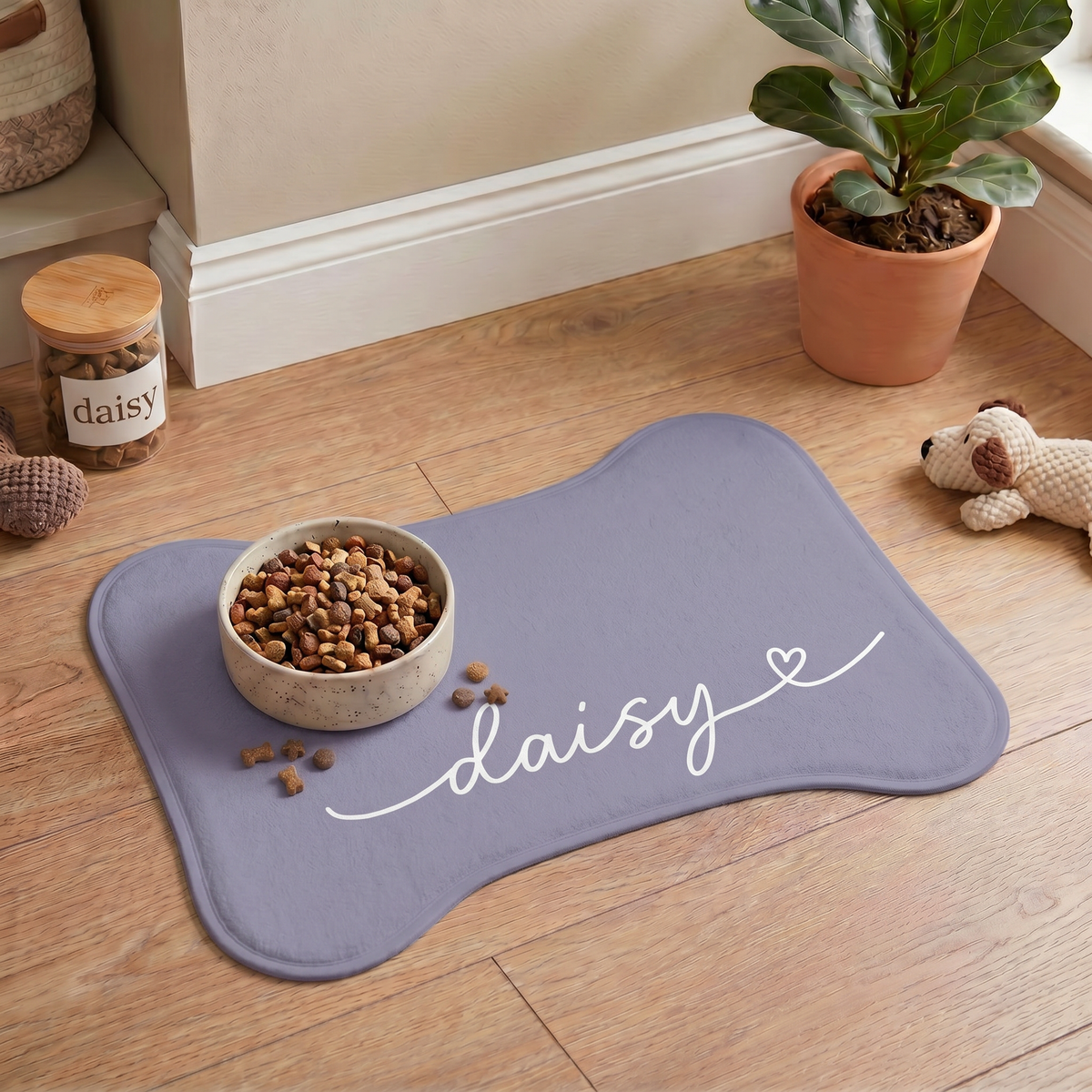 Lavender bone-shaped personalized pet feeding mat with a food bowl on a wooden floor next to houseplants