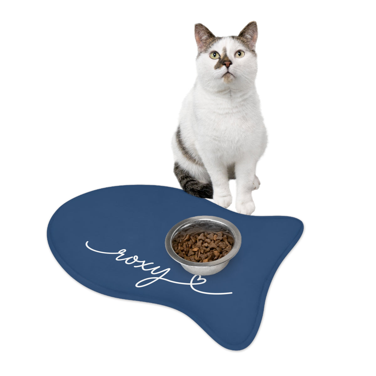 Cat sitting on a midnight blue fish-shaped personalized pet feeding mat next to a food bowl