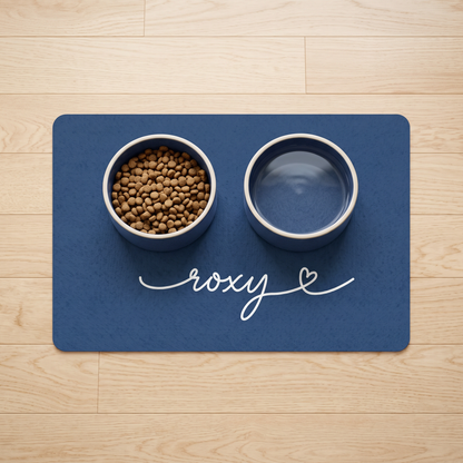 Midnight blue personalized pet food mat with the name Roxy holding a food bowl and a water bowl on a wooden floor