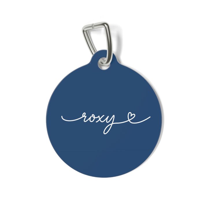 Round midnight blue personalized pet tag with the name Roxy in white handwritten script and a small heart