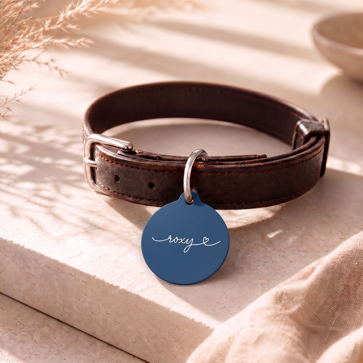 Midnight blue personalized pet tag on a dark leather collar resting on a table