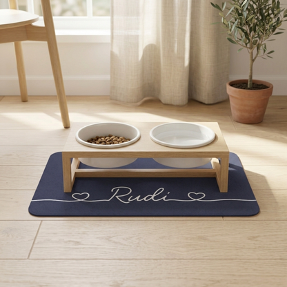 Elevated wooden pet feeder on a navy blue personalized pet food mat by a window