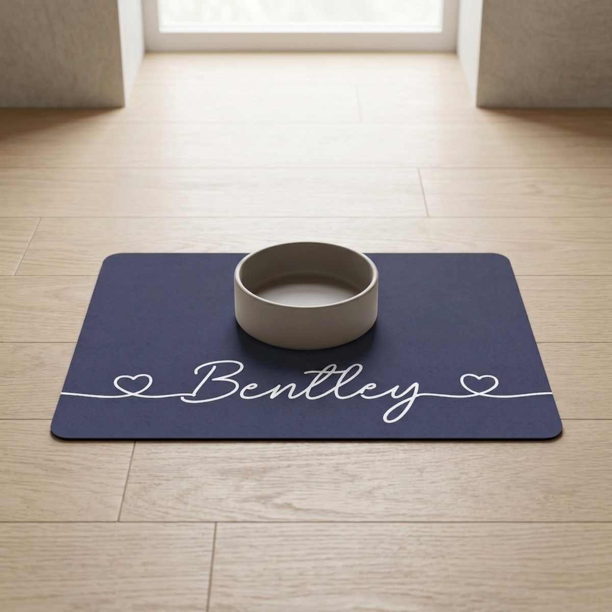 Navy blue personalized pet food mat with the name Bentley and a bowl in a bright room