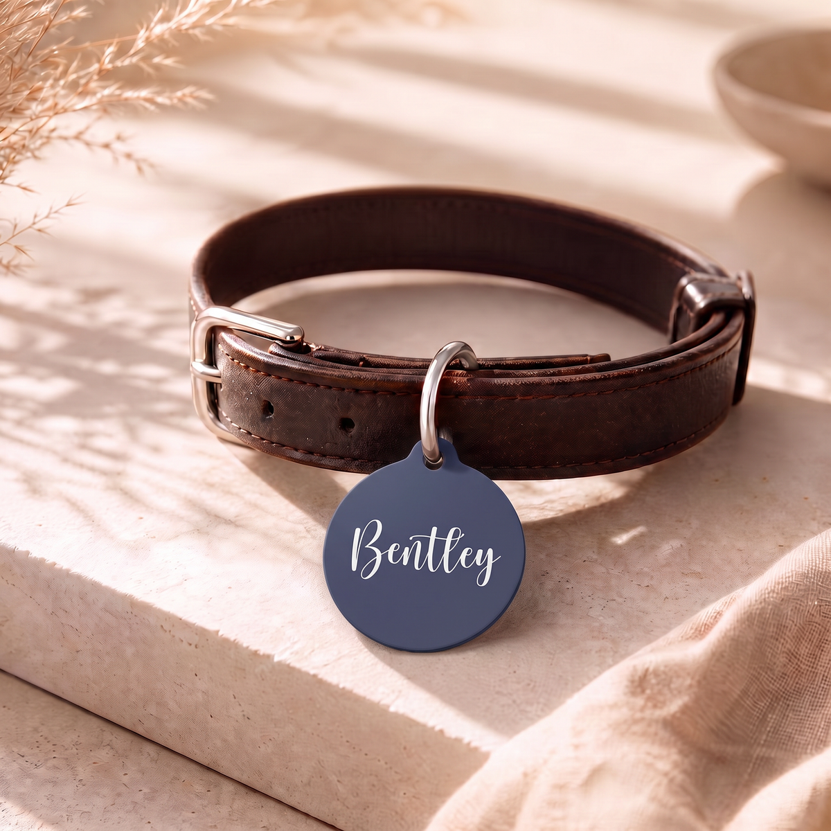 Navy blue personalized pet tag on a dark leather collar resting on a table
