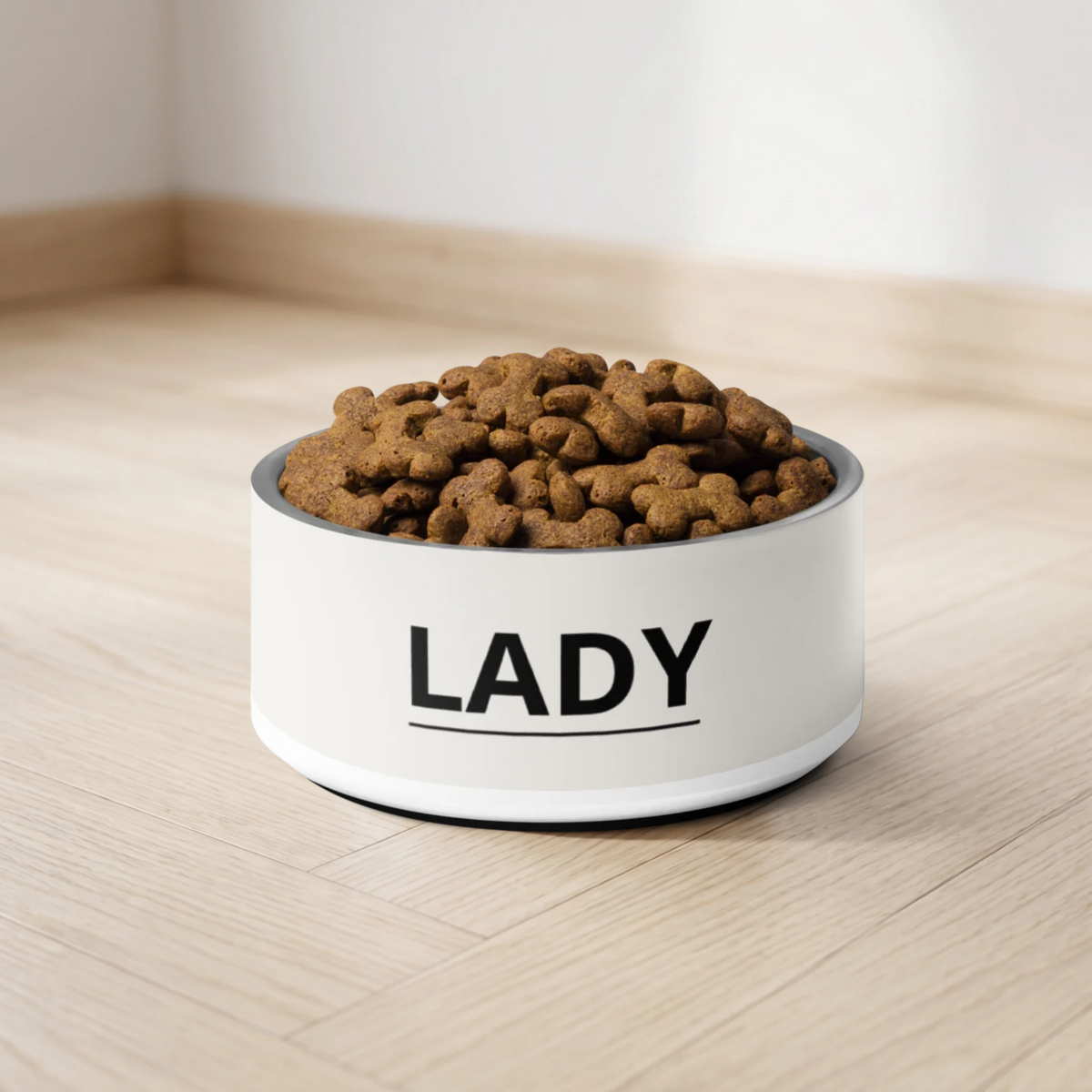 Close-up of an off-white modern personalized dog bowl with the name Lady filled with kibble on a wooden floor
