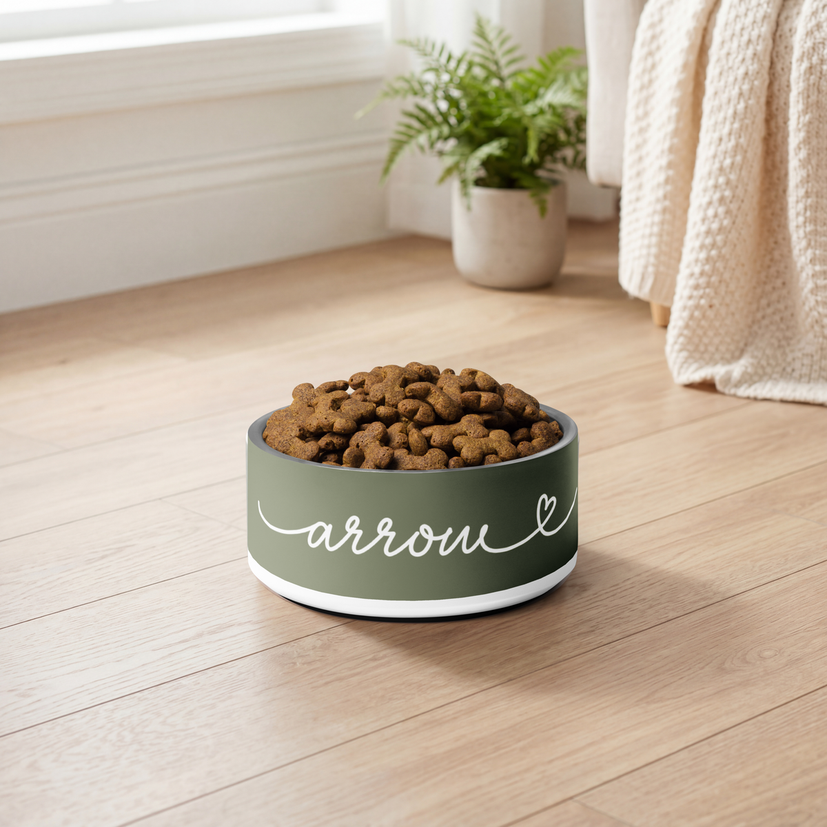 Olive green personalized dog bowl with kibble on a wooden floor by a window
