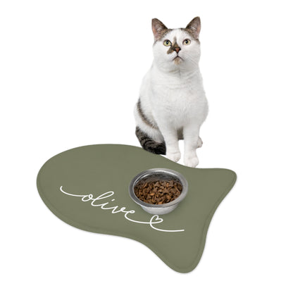 Cat sitting on an olive green fish-shaped personalized pet feeding mat next to a food bowl